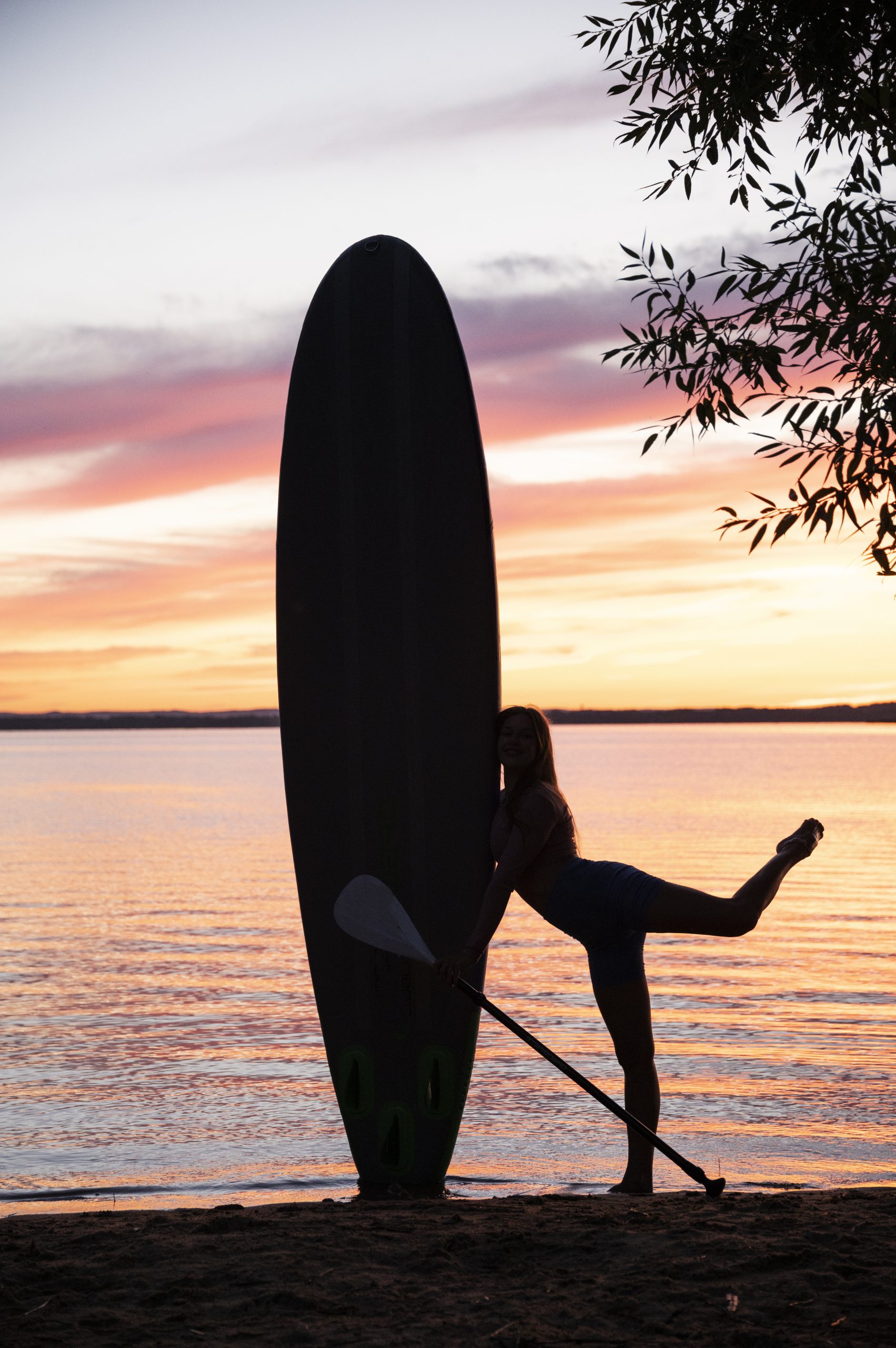 Chica caminando con tabla de surf por la playa al atardecer en Loredo